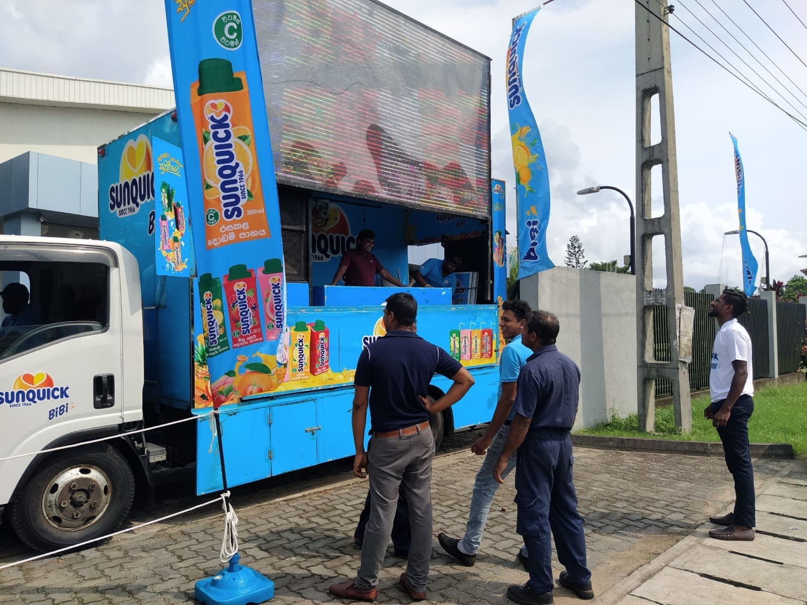 Sunquick branded promotion truck flanked by printed feather flags