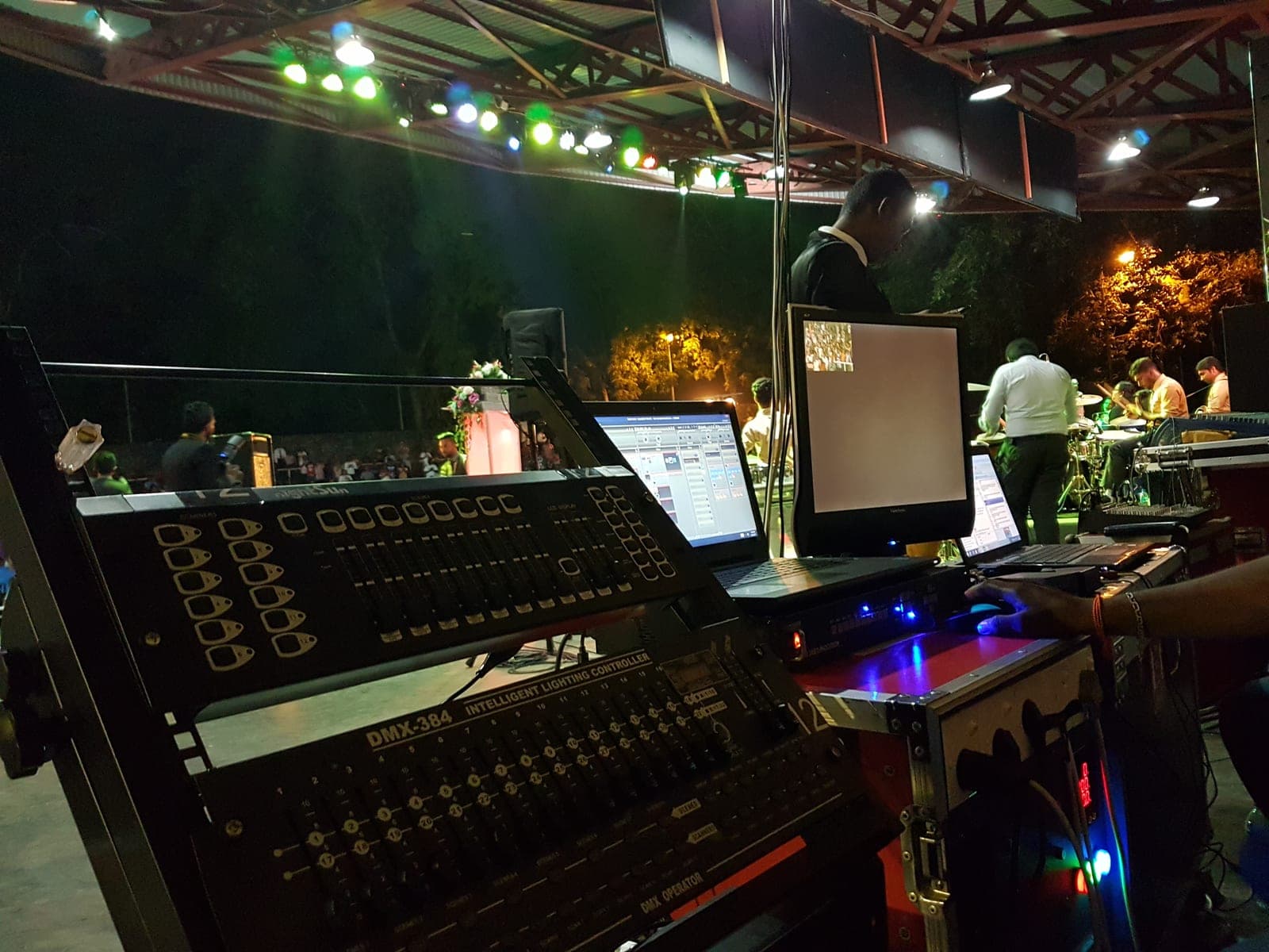 Sound-mixing console with stage lighting behind, at night