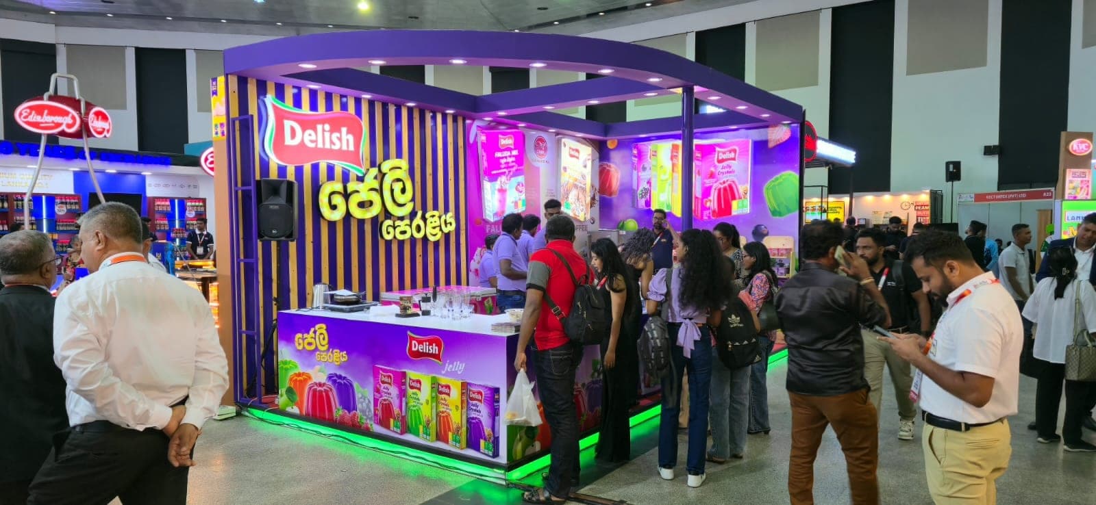 Delish exhibition stall busy with visitors, lit purple fascia above