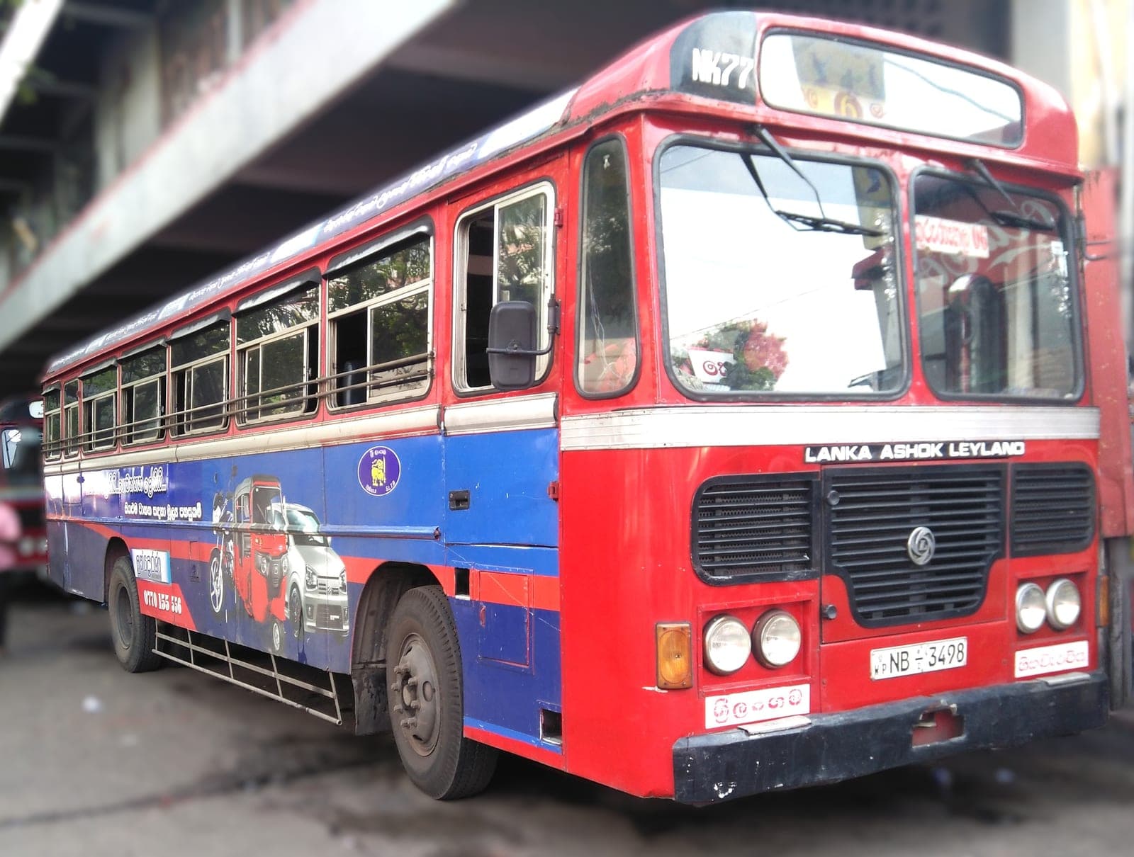 Route bus in red-and-blue printed livery, front three-quarter view